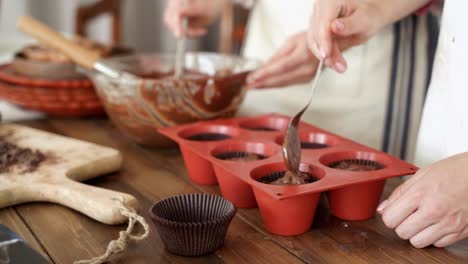 Pareja-Colocando-La-Masa-De-Cupcakes-De-Chocolate-En-El-Molde-Para-Hornear,-Cerca-De-Dos-Personas-Preparando-Muffins