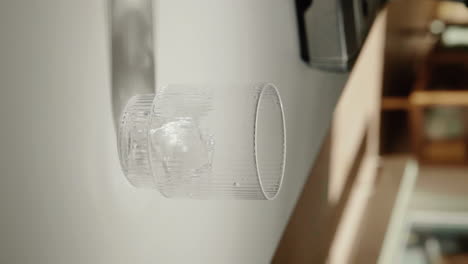 Vertical-Video-hand-putting-ice-cubes-into-beautiful-drinking-glass-at-home