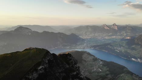 Aerial-flight-around-the-summit-of-Niederbauen-Chulm-on-a-golden-summer-evening-in-the-Swiss-Alps-with-a-view-of-Mythen,-Rigi,-Burgenstock,-Pilatus-and-glowing-cliffs-above-Lake-Lucerne