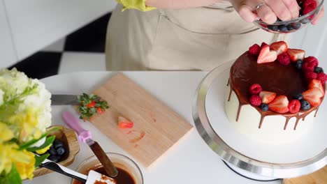 Top-view-of-a-woman-decorating-a-chocolate-cake-with-strawberry-fruits,-pastry-chef-working-in-the-kitchen