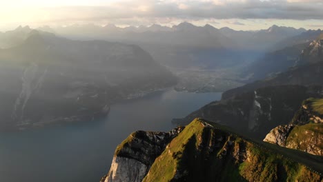 Aerial-flyover-alongside-of-the-cliffs-at-Niederbauen-Chulm-in-Uri,-Switzerland-with-a-view-of-Lake-Lucerne-and-its-fjords-on-a-golden-summer-morning-in-Swiss-Alps