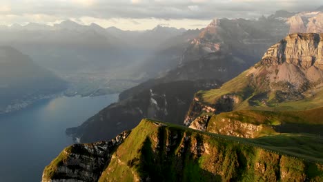 Aerial-flight-around-the-summit-of-Niederbauen-Chulm-on-a-golden-summer-morning-in-the-Swiss-Alps-with-a-spinning-view-of-the-fjords-of-Lake-Lucerne,-Uri,-Mythen,-Rigi,-Burgenstock-and-the-rising-sun
