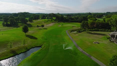 Aerial-drone-shot-of-a-golf-hole-with-fairway-bunkers-at-a-country-club-with-sprinklers-running