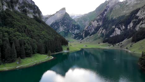 Aerial-flyover-over-the-water-of-lake-Seealpsee-in-Appenzell,-Switzerland-with-a-reflection-of-the-Alpstein-peaks-on-the-lake-with-reverse-motion-toward's-the-shore