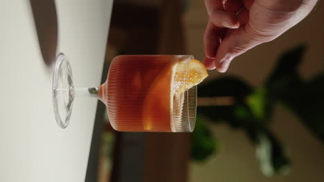 Vertical-Video-Placing-an-orange-slice-to-decorate-espresso-tonic-in-a-beautiful-drinking-glass-at-home