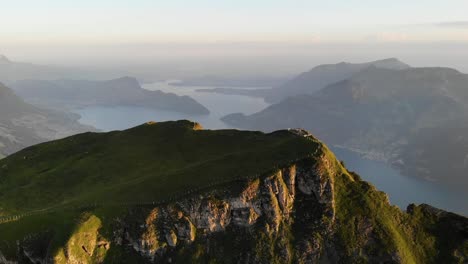 Aerial-view-of-Niederbauen-Chulm-in-Uri,-Switzerland-with-view-of-the-peak's-cliffs-and-Lake-Lucerne,-Burgenstock,-Pilatus-plus-Rigi-in-the-background-on-a-golden-summer-morning-in-the-Swiss-Alps