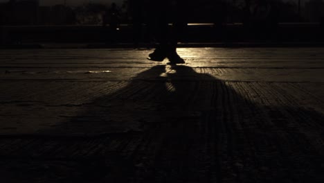 Shadow-of-a-person-walking-across-a-street-or-sidewalk-at-night-with-a-light-reflecting-off-the-pavement---slow-motion