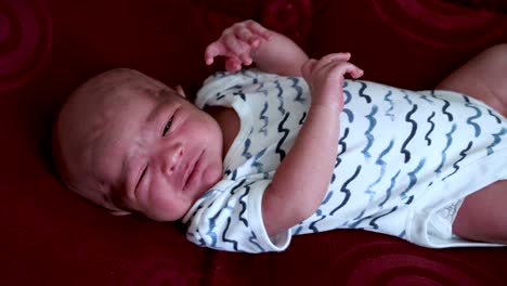 Indian-Newborn-Baby-Boy-Looking-Grumpy-And-Crying-In-Bodysuit-Laid-Down-On-Bed