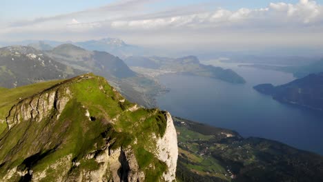 Aerial-flyover-towards-Niederbauen-Chulm-in-Uri,-Switzerland-with-a-view-of-cows-grazing-and-mountain-peak's-tall-cliffs-above-Lake-Lucerne-on-a-summer-morning-in-the-Swiss-Alps