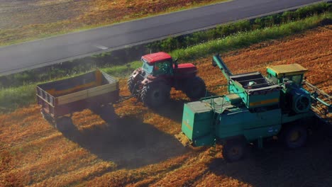 Agricultural-Machinery-On-Wheat-Field-In-Summer---Combine-Harvester-Will-Load-Truck-With-Harvested-Grain---drone-shot
