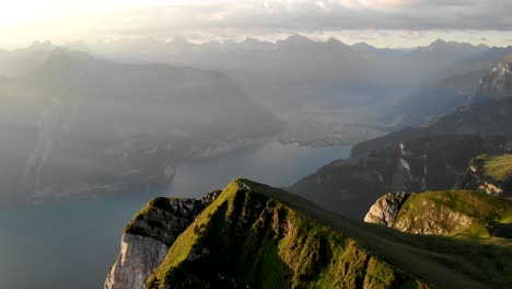 Aerial-flyover-over-the-summit-of-Niederbauen-Chulm-with-Lake-Lucerne,-Uri-and-lakeside-fjords-and-cliffs-in-view-on-a-golden-summer-morning-in-the-Swiss-Alps