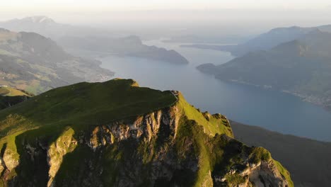 Aerial-flyover-over-the-summit-of-Niederbauen-Chulm-with-a-view-of-Lake-Lucerne,-Burgenstock-and-Pilatus-in-the-background-on-a-golden-summer-morning-in-the-Swiss-Alps