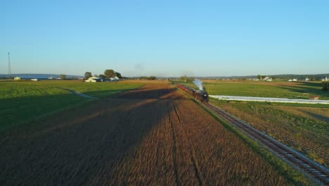 A-Drone-View-of-an-Antique-Steam-Passenger-Train-Blowing-Smoke-and-Steam-Traveling-Thru-Fertile-Corn-Fields-During-the-Golden-Hour-in-Slow-Motion-on-a-Sunny-Summer-Day
