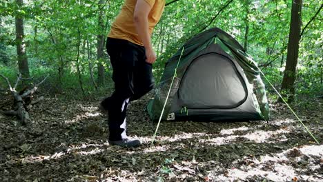 Person-adjusting-tent-while-camping-forest-area,-back-view
