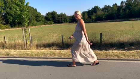 Slow-motion-shot-of-pregnant-blond-woman-walking-with-flip-flop-on-rural-road-during-sunny-day---close-up---Beautiful-pretty-smiling-young-girl-before-birth