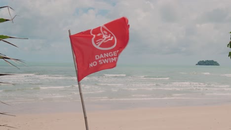 No-Swimming-Red-flag-bloowing-in-the-wind-at-tropical-beach,-Horizon-over-water
