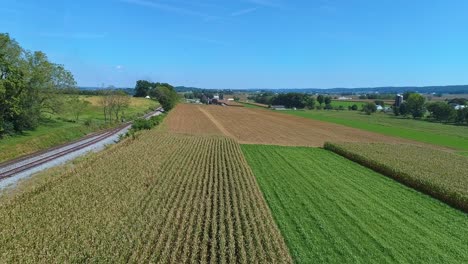 Eine-Drohnenansicht-Von-Ackerland-Und-Maispflanzen,-Die-Darauf-Warten,-An-Einem-Herbsttag-Entlang-Einer-Eisenbahnstrecke-Geerntet-Zu-Werden