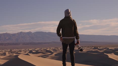 Slowmotion-video-of-hooded-photographer-standing-on-sand-dunes-yelling-into-the-vast-distance-of-blue-sky-and-vast-space-in-death-valley-california-alone