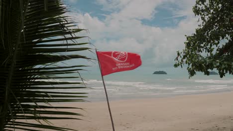 Playa-Tropical-Con-Bandera-Roja-Que-Advierte-Que-No-Se-Puede-Nadar,-Palmeras-En-Primer-Plano,-Paisaje-Escénico