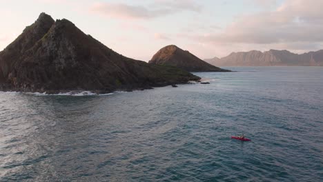 Man-on-red-kayak-paddling-toward-Na-Mokulua-Hawaiian-islands-at-dusk,-Hawaii