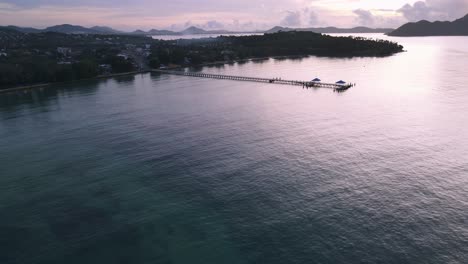 Drone-aerial-pan-up-over-blue-ocean-to-pier-during-sunrise