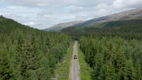 Drone-Following-SUV-With-Camper-On-Rooftop-Driving-Offroad-Through-Evergreen-Forest-In-Lomsdal-Visten,-Norway