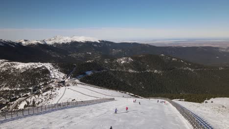 Stabilized-shot-of-a-snowy-mountain-side-while-people-are-skiing-on-a-sunny-winter-day