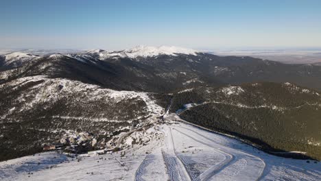 Rising-aerial-establishing-shot-over-a-ski-track-on-the-top-of-a-snowy-mountain