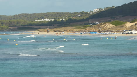 Ein-Entfernter-Blick-Auf-Einen-Menorca-Strand-Mit-Kleinen-Wellen-Und-Unkenntlich-Schwimmenden-Touristen