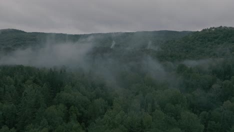 Drone-flying-through-a-beautiful-foggy-mountain-top-landscape,-pullout-reveal
