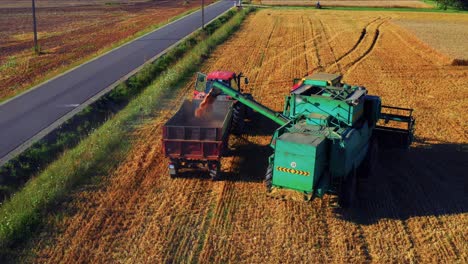 A-Combine-Harvester-Unloads-Grains-Into-A-Farm-Truck-During-Harvest---drone-shot
