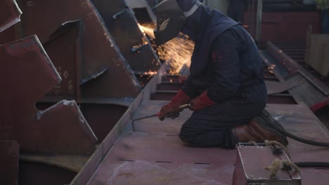 Man-working-on-a-cargo-ship-is-hammering-a-spot-he-just-welded-to-make-it's-form-good