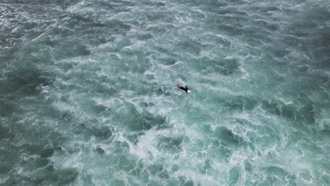Aerial-drone-shot-of-surfers-swimming-over-big-waves-at-Playa-Meron-Beach-in-San-Vicente-de-la-Barquera