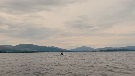 Young-Man-Paddleboarding-Away-From-The-Shoreline-Of-Loch-Lomond-Exploring-The-Views