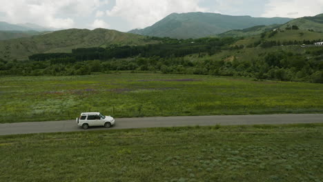 White-Four-wheel-SUV-Car-Driving-On-The-Road-Passing-By-Green-Grassland-And-Mountains-Near-Aspindza-In-Georgia