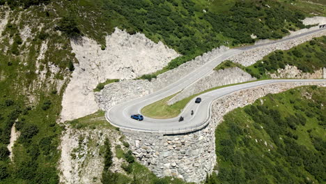 Tracking-panoramic-aerial-shot-of-some-cars-and-motos-circulating-through-a-very-tight-curve-in-Grimselpass,-Switzerland