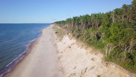 Aerial-view-of-Baltic-sea-beach-at-Jurkalne-on-a-sunny-day,-white-sand-cliff-damaged-by-waves,-coastal-erosion,-climate-changes,-wide-angle-drone-shot-moving-backward
