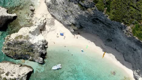 Drone-zooms-in-on-the-beach-at-Tremiti-Island,-where-people-can-be-seen-swimming-and-strolling-down-the-shore