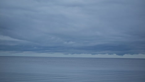 -Timelapse-shot-of-movement-of-thick-clouds-over-blue-sea-water-along-shoreline-at-daytime