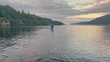Young-Woman-In-A-Wetsuit-Paddleboarding-On-A-Stand-Up-Paddleboard-Into-The-Sunny-Horizon-On-Loch-Ness