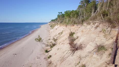 Aerial-view-of-Baltic-sea-beach-at-Jurkalne-on-a-sunny-day,-white-sand-cliff-damaged-by-waves,-coastal-erosion,-climate-changes,-wide-angle-drone-shot-moving-forward-close-to-the-cliff