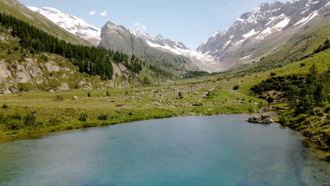 Luftaufnahme,-Die-Im-Sommer-Durch-Einen-Bergsee-Mit-Türkisfarbenem,-Klarem-Wasser-Vorrückt,-Mit-Schneebedeckten-Bergen-Im-Hintergrund