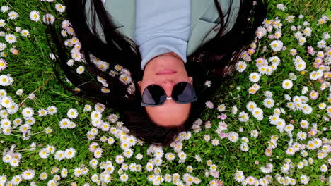 A-beautiful-woman-lying-down-in-a-bed-a-daisies-with-flowers-in-her-long-black-hair---looking-up-wearing-sunglasses
