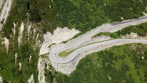 Two-white-cars-and-a-moto-circulating-on-a-very-tight-curve-in-Grimselpass,-Switzerland