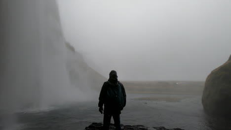 Cinematic-shot-behind-the-Icelandic-waterfall-Seljalandsfoss-and-where-a-man-admires-the-beauty-and-strength-of-the-falling-water