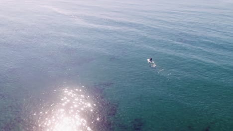 Drone-flying-on-the-Mediterranean-sea,-birds-eye-view-over-a-paddleboarder-rotating-into-the-horizon