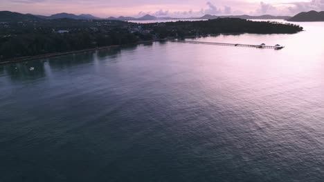 Drone-aerial-during-sunrise-over-tropical-Thailand-beach-with-pier-pan-down