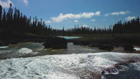 Low-flyover-above-waves-from-Pacific-Ocean-flowing-into-natural-pool-of-Oro,-Isle-of-Pines