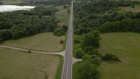 Aerial-shot-of-the-long-highway-with-driving-cars-surrounded-by-green-lush-trees-from-both-sides