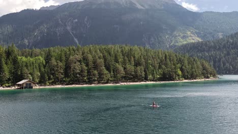 People-Stand-up-Paddle-board-on-a-Lake-Blindsee-in-the-Mountains-in-Austria-Tyrol,-Hut-by-the-Lake-in-background